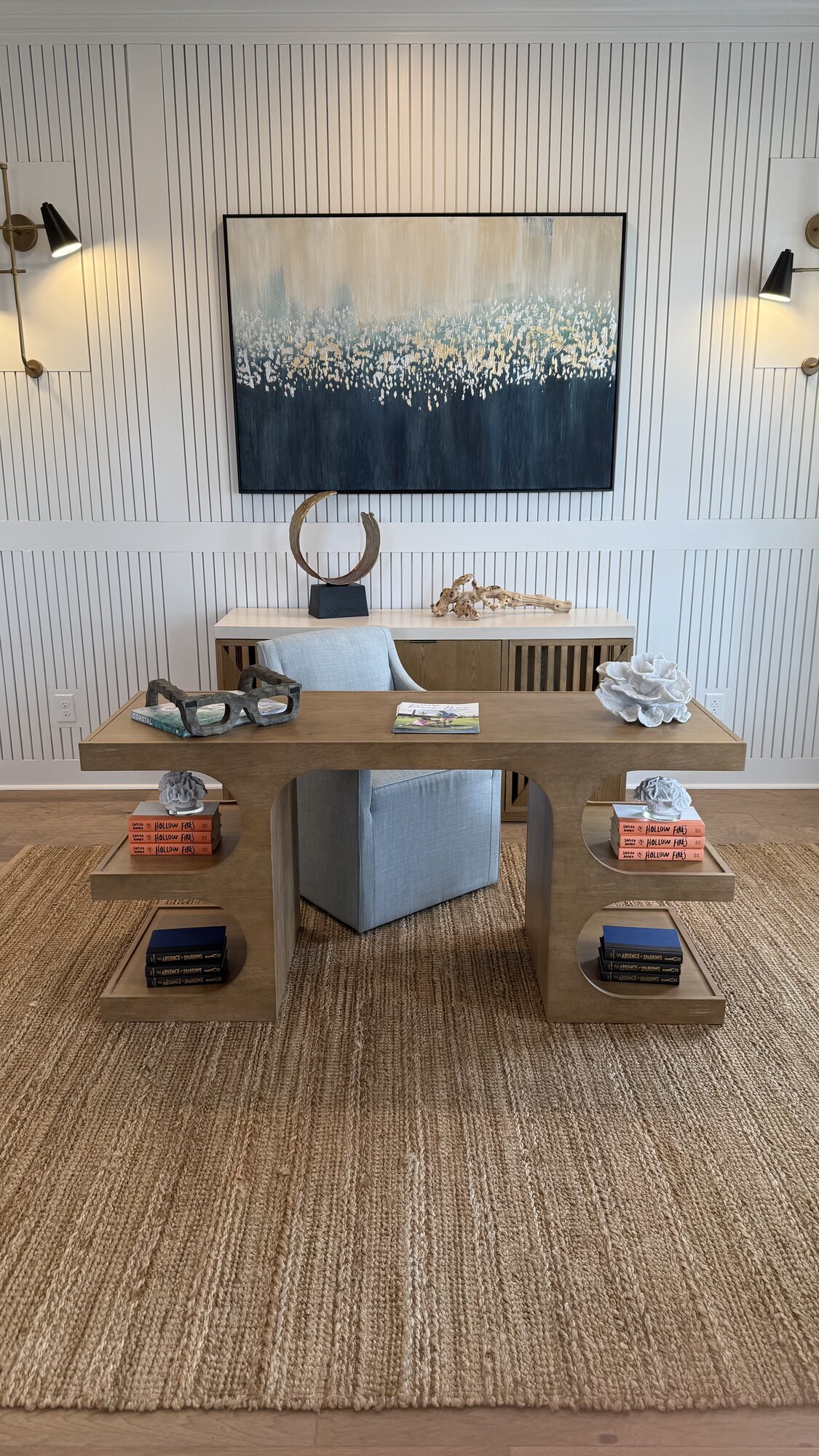 Quiet home office with paneled walls, jute rug, and brass sconces